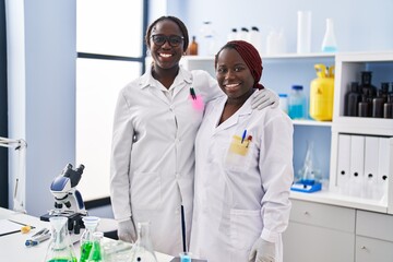 Obraz premium Two african women working at scientist laboratory looking positive and happy standing and smiling with a confident smile showing teeth