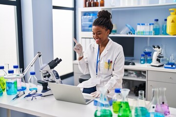 Young african american with braids working at scientist laboratory with laptop smiling happy...