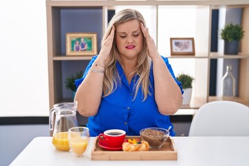 Obraz na płótnie Canvas Caucasian plus size woman eating breakfast at home with hand on head for pain in head because stress. suffering migraine.