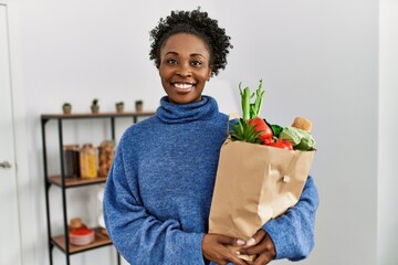 African american woman smiling confident holding groceries bag at home