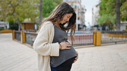 Young pregnant woman smiling confident touching belly at park