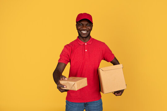 Glad friendly millennial black man courier in red uniform give box for client