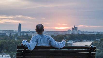 Fototapeta na wymiar A man sitting on a bench watching the sunset over the city and river
