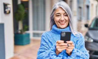Fototapeta na wymiar Middle age grey-haired woman smiling confident using smartphone at street