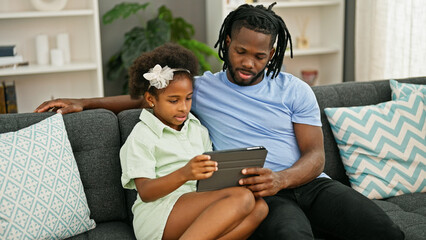 African american father and daughter using touchpad sitting on sofa at home