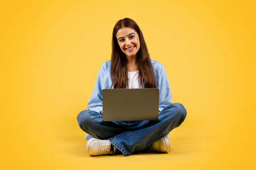 Positive caucasian young student lady use laptop, typing, work and sit on floor