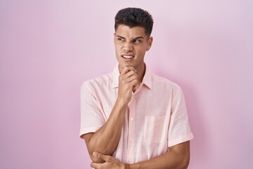 Young hispanic man standing over pink background thinking worried about a question, concerned and nervous with hand on chin