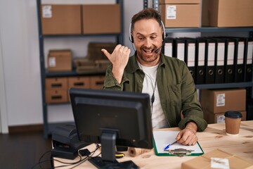 Middle age caucasian man working at small business ecommerce wearing headset pointing thumb up to the side smiling happy with open mouth