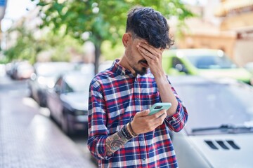 Young hispanic man using smartphone with worried expression at street