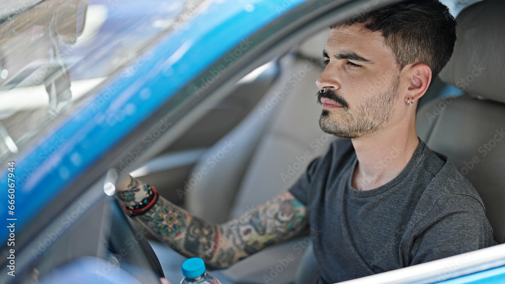 Wall mural Young hispanic man driving car with relaxed expression at street