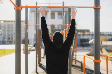 a handsome healthy athletic guy doing callsthenics pull-ups outdoor on a sports ground