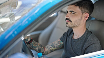 Young hispanic man driving car with relaxed expression at street