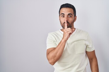 Hispanic man with beard standing over isolated background asking to be quiet with finger on lips. silence and secret concept.