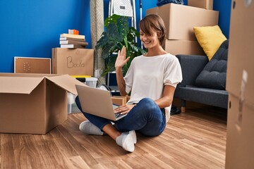 Young beautiful hispanic woman having video call sitting on floor at new home