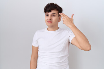 Young non binary man wearing casual white t shirt shooting and killing oneself pointing hand and fingers to head like gun, suicide gesture.