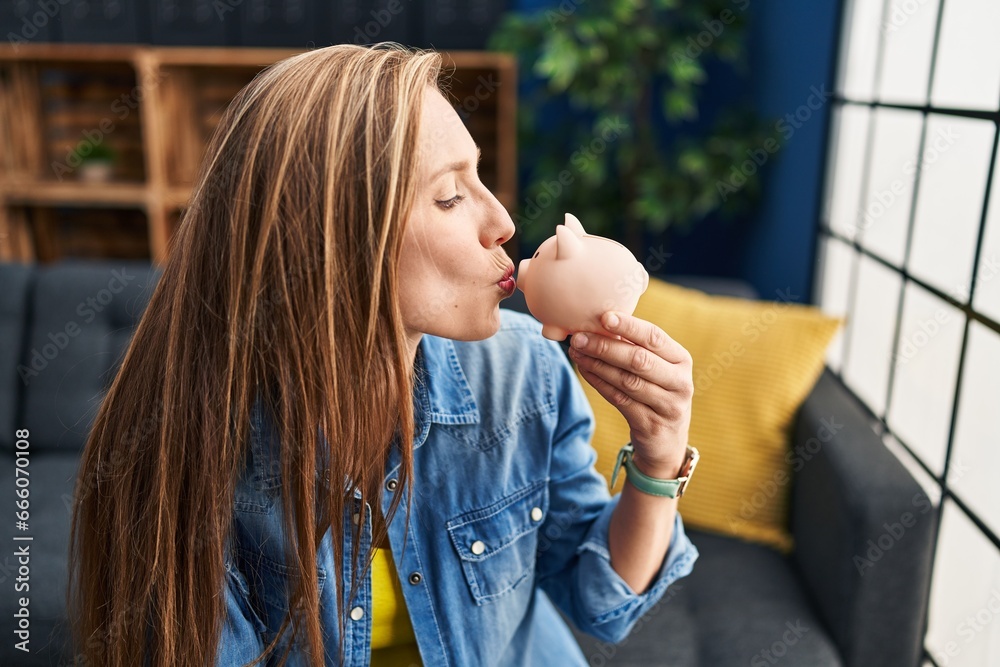 Canvas Prints young blonde woman holding piggy bank sitting on sofa at home