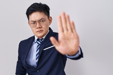 Young asian man wearing business suit and tie doing stop sing with palm of the hand. warning expression with negative and serious gesture on the face.