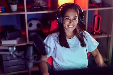 Young beautiful hispanic woman streamer smiling confident sitting on table at gaming room