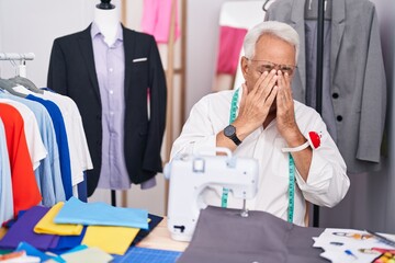 Middle age man with grey hair dressmaker using sewing machine rubbing eyes for fatigue and...
