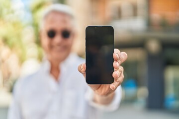 Middle age grey-haired man smiling confident showing screen smartphone at street