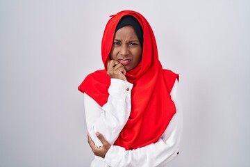 Young arab woman wearing traditional islamic hijab scarf looking stressed and nervous with hands on mouth biting nails. anxiety problem.