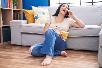Young beautiful hispanic woman talking on smartphone drinking coffee at home