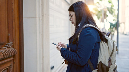 Young hispanic woman tourist wearing backpack using smartphone looking for address at street