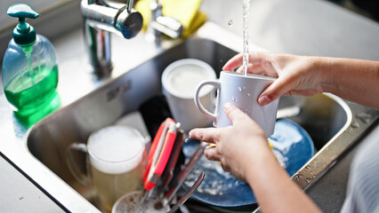 Young beautiful hispanic woman washing plates at the kitchen
