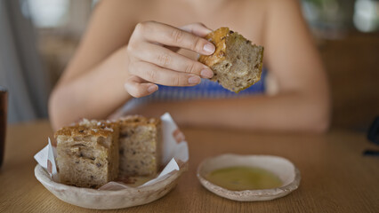 Young hispanic woman dipping bread into olive oil at the restaurant