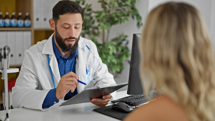 Obraz premium Young hispanic man doctor writing medical report to patient at the clinic