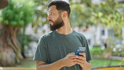 Young hispanic man using smartphone with serious expression at park