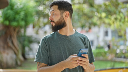 Fototapeta premium Young hispanic man using smartphone with serious expression at park