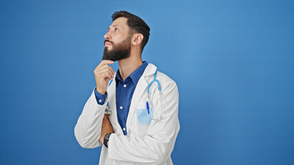 Young hispanic man doctor standing with doubt expression thinking over isolated blue background