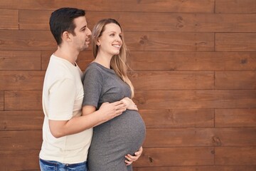 Man and woman couple hugging each other expecting baby over isolated wooden background - obrazy, fototapety, plakaty