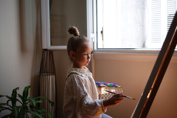 little cute girl draws with paints on canvas at the easel. the concept of early development of...