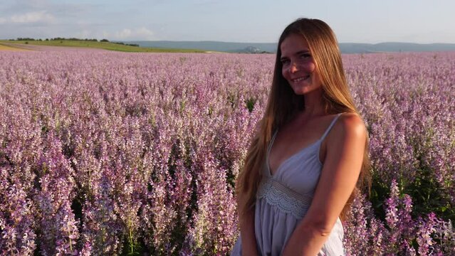 A young woman with long hair gently in the sage bushes. Field of Clary sage - Salvia Sclarea in bloom, cultivated to extract the essential oil and honey. Close up. Selective focus.