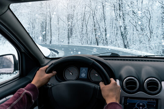 A man is driving a car on a winter road in a blizzard.