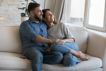 Happy dating couple enjoying relaxation, leisure time at cozy home, discussing romantic plans, dreaming together, looking at window away, holding hands, hugging with love, affection