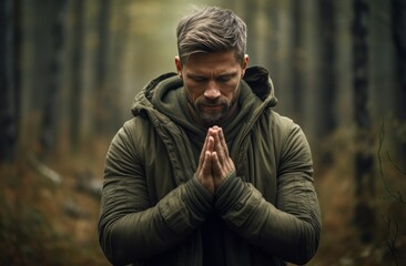 Man praying in distressed woods, wrists crossed Pastoral setting