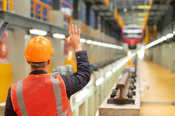 Rear view of electric train industry engineer wearing a safety helmet and reflective vest. There is an electric car in the car repair factory as the background image.