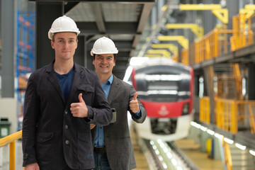 Portrait of two young engineers showing thumbs up in front of train station