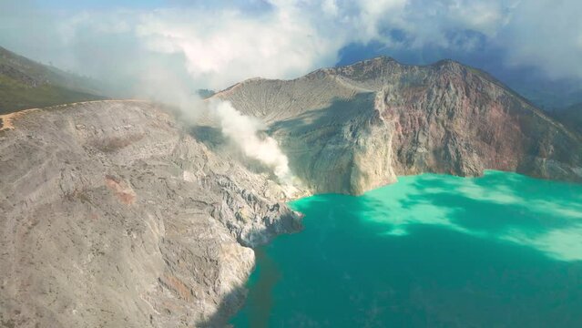 Active volcano Kawah Ijen in the crater with sulfur lake turquoise color and smoke emissions from burning sulfur, East Java, Indonesia. Aerial Drone view 4K.