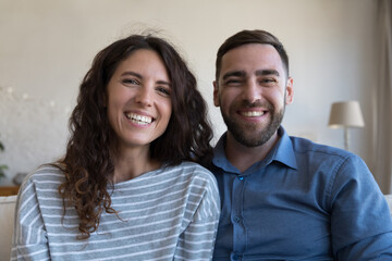 Happy joyful dating couple home head shot portrait. Husband and wife sitting close, looking at camera with toothy smiles, laughing, talking on video call, chatting, enjoying romantic relationship