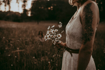 Frau läuft über Wiese und hält weiße Blumen als Strauß