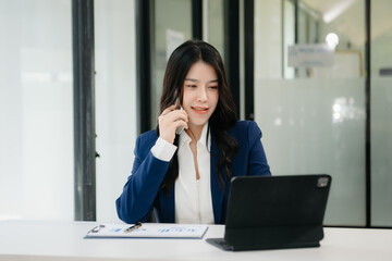 Confident business expert attractive smiling young woman typing laptop ang holding digital tablet on desk in creative office.