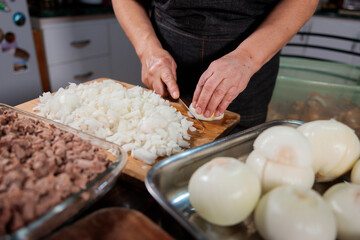 Close up of unrecognizable latin woman chopping onion and meat for filling chilean baked empanadas. Domestic kitchen