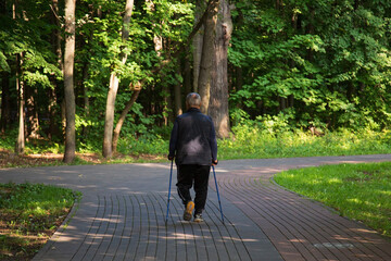 An elderly man is engaged in Nordic walking in the park.