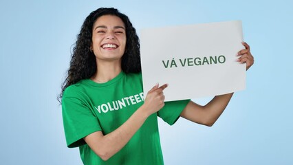 Volunteer woman, vegan poster and studio for smile on face, search and point by blue background. Recruitment, choice and call to action for sustainable food, diet and eco friendly diet in Barcelona