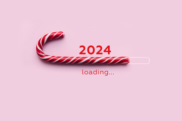 Striped candy cane and lettering 2024 loading on pink background. Concept of waiting for seasonal holidays. Copy space, selective focus