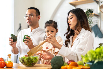 Portrait of enjoy happy love asian family father and mother with little asian girl daughter child having fun help cooking food healthy eat together with fresh vegetable salad ingredient in kitchen